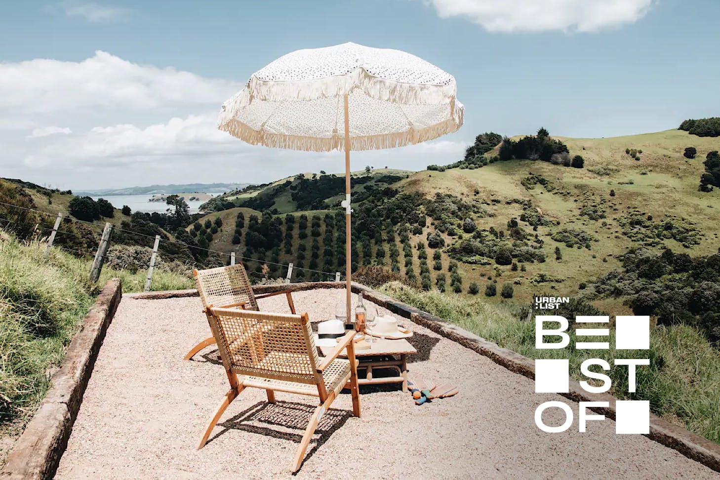 A darling chair and umbrella set up overlooking rolling hills and the ocean at Fleetwood, one of the best Airbnbs on Waiheke Island.